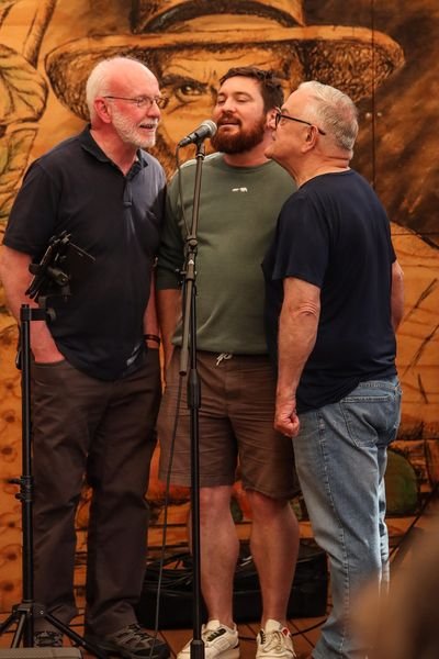 The Stovies, Neil, Graeme and Bob, singing together into a single microphone at Spreyton Cider Co in Tasmania